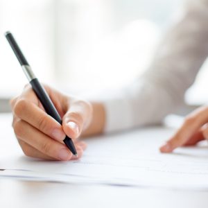 Hand of young businesswoman writing on paper or signing contract at table in office